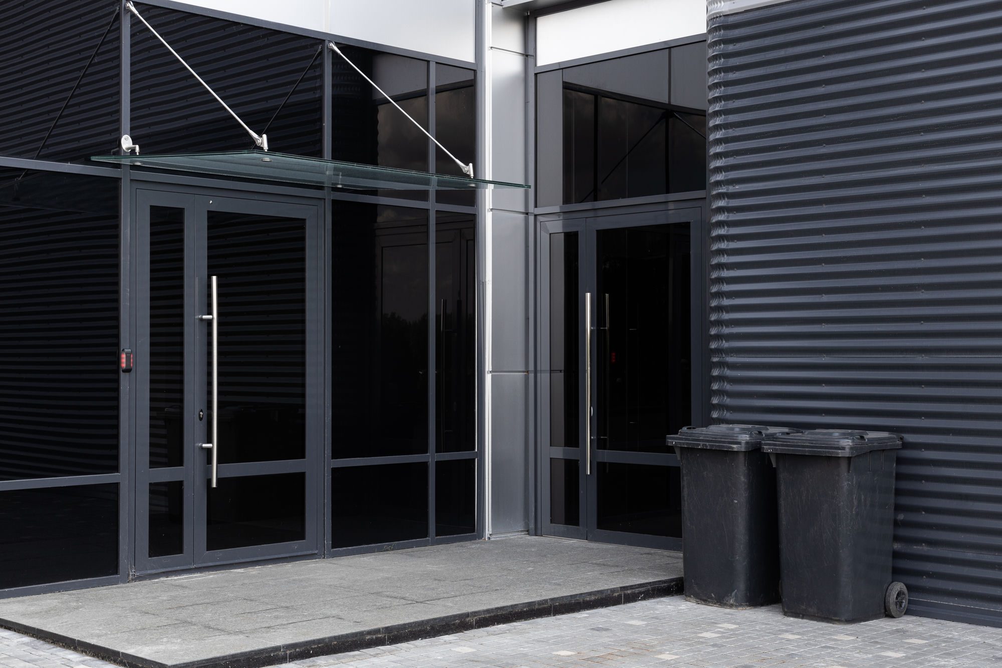 Commercial wheelie bins beside the glass entrance of a modern business unit Commercial wheelie bins beside the glass entrance of a modern business unit